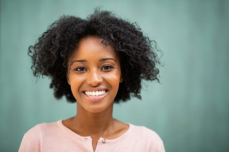 Una joven negra sonriendo frente a un fondo verde en Miami Designer Smiles.