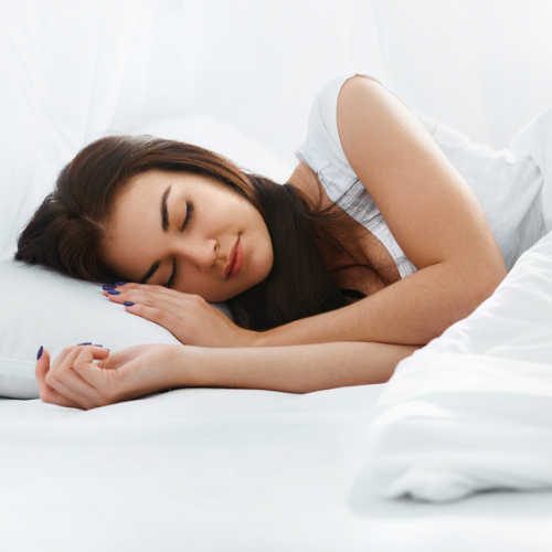 Una joven durmiendo en una cama blanca antes de su cita con el Dr. Raúl García, dentista general y dentista cosmético.