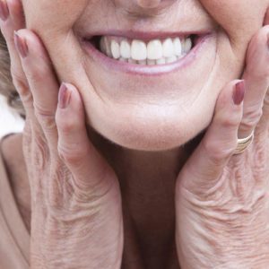 Una mujer con dentadura postiza permanente sonríe con las manos en la cara.