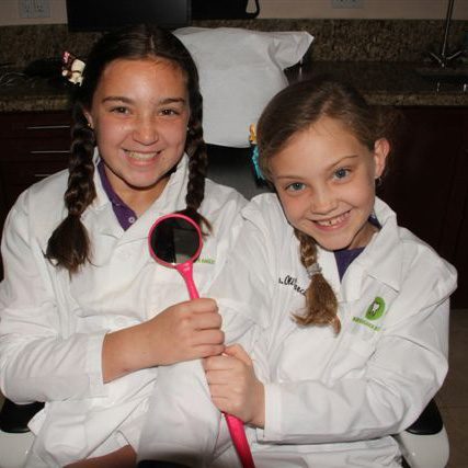 Dos niñas con batas de laboratorio posan para una fotografía en Miami Designer Smiles con el Dr. Raúl García.