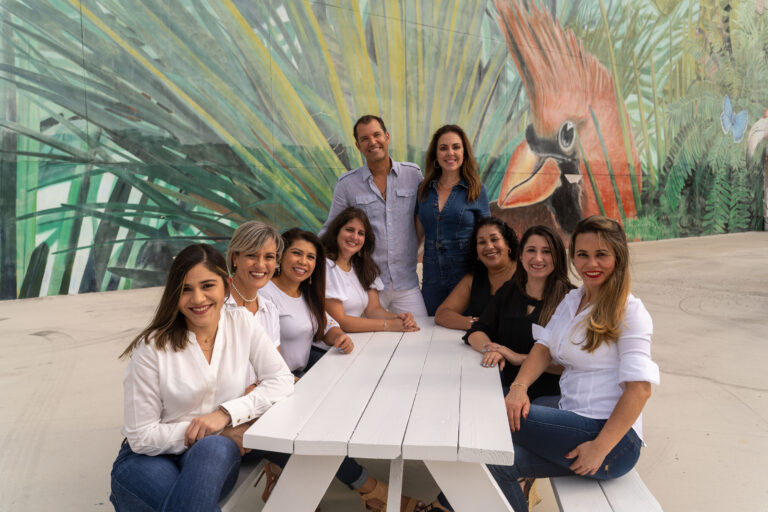 A group of women sitting at a table in front of a mural, discussing dental implants.