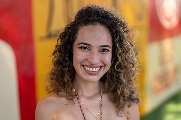A woman with curly hair smiling in front of a colorful wall, resembling a cheerful member of a Dental Team.