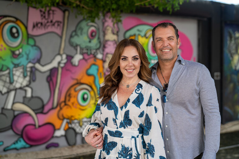 Un hombre y una mujer recibiendo una intervención de ortodoncia frente a una pared cubierta de graffiti.