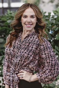 Una mujer con una blusa floral rosa y pantalones negros.