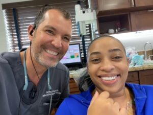 Two individuals smiling for a selfie in a dental office.