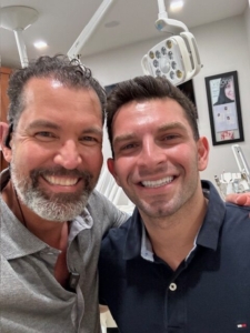 Two men smiling for a selfie in a dental office.