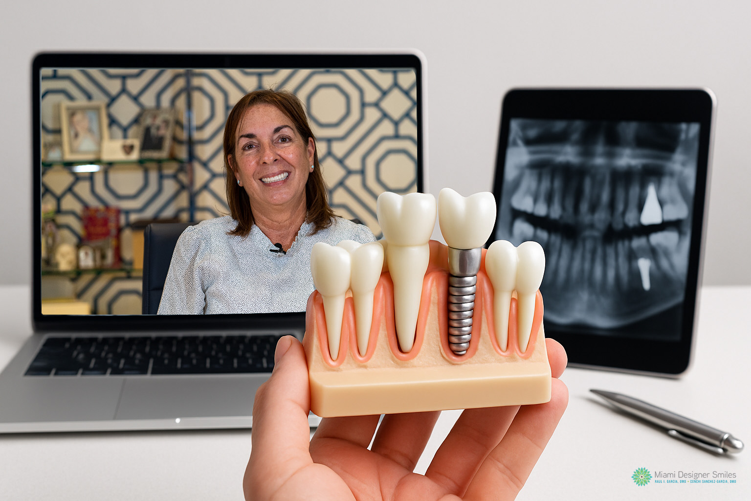 A hand holds a dental implant model in front of a laptop displaying a smiling woman and a tablet showing a dental X-ray, showcasing the possibilities of virtual cosmetic dental consultations.